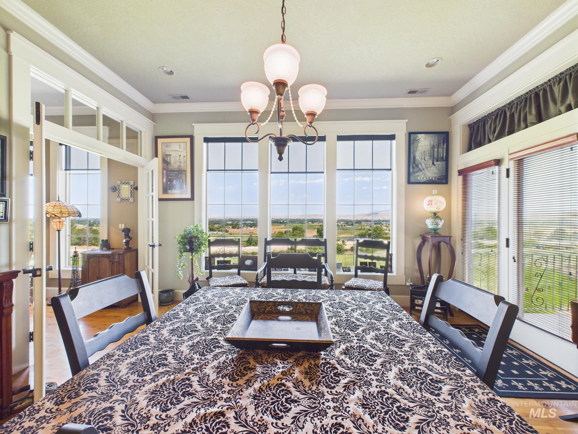 Dining area featuring plenty of natural light, ornamental molding, a chandelier, wood finished floors, and french doors