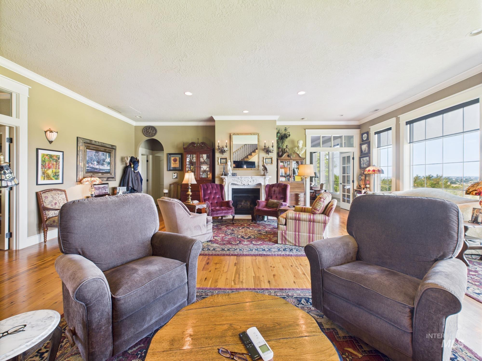 Living area featuring crown molding, wood finished floors, a glass covered fireplace, arched walkways, and a textured ceiling