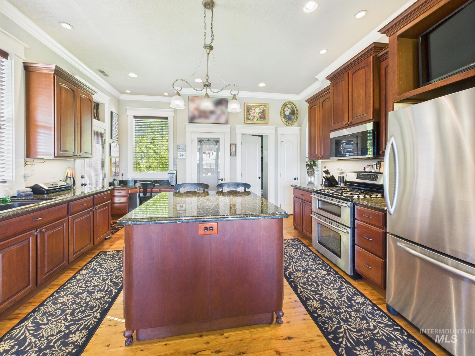 Kitchen featuring appliances with stainless steel finishes, a center island, dark brown cabinets, light wood-style flooring, and ornamental molding