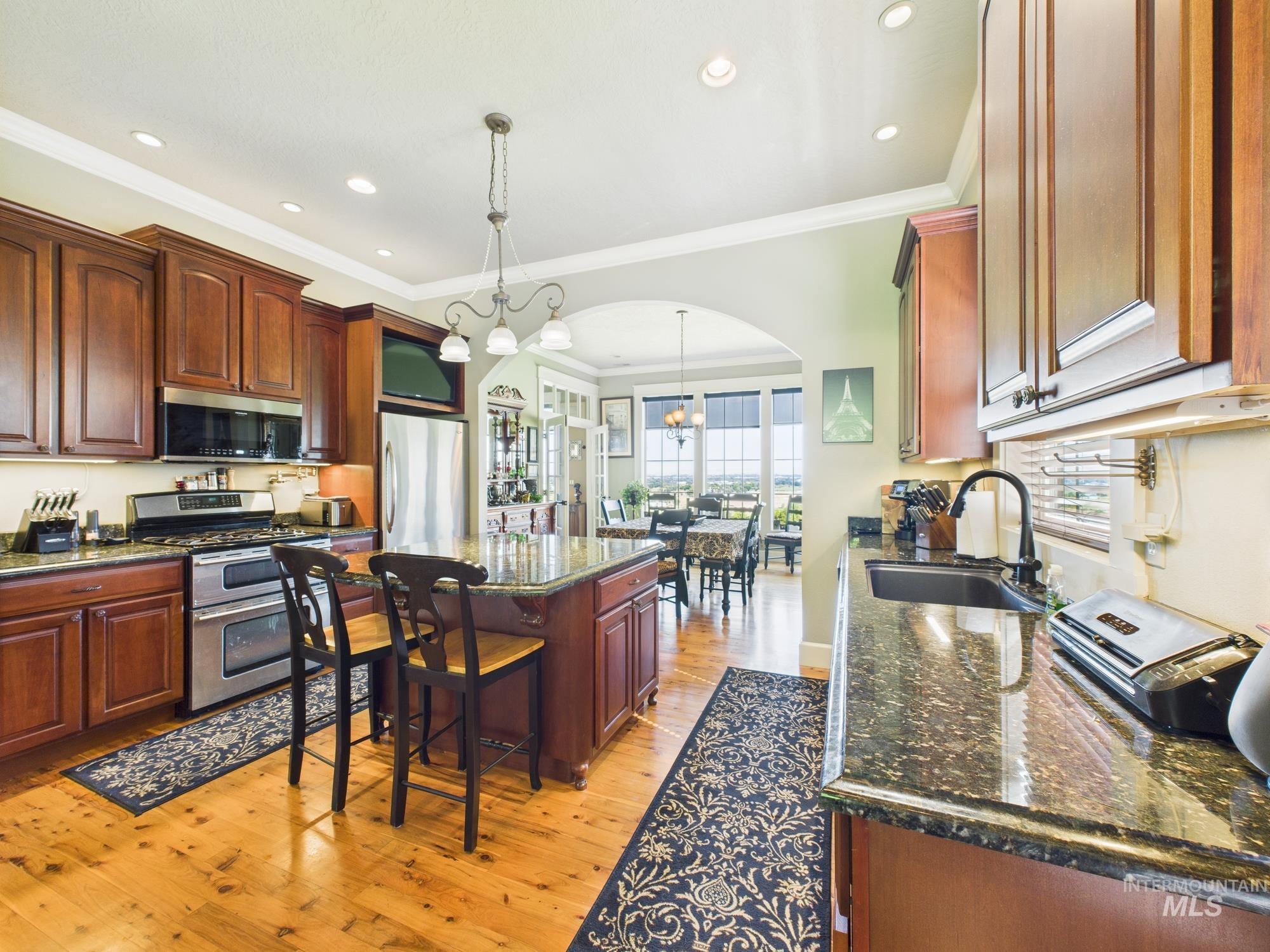 Kitchen featuring stainless steel appliances, arched walkways, a center island, light wood-type flooring, and ornamental molding