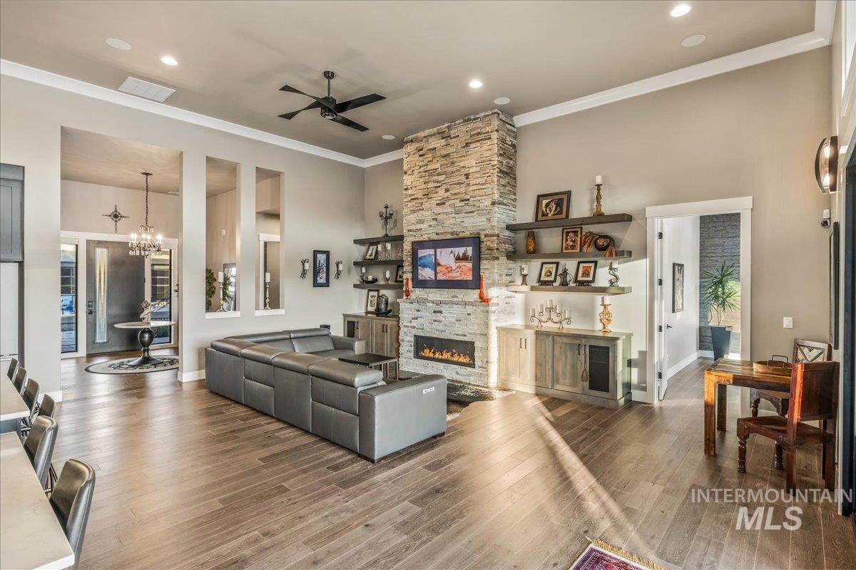 Living area with a fireplace, ceiling fan, crown molding, a chandelier, and wood finished floors