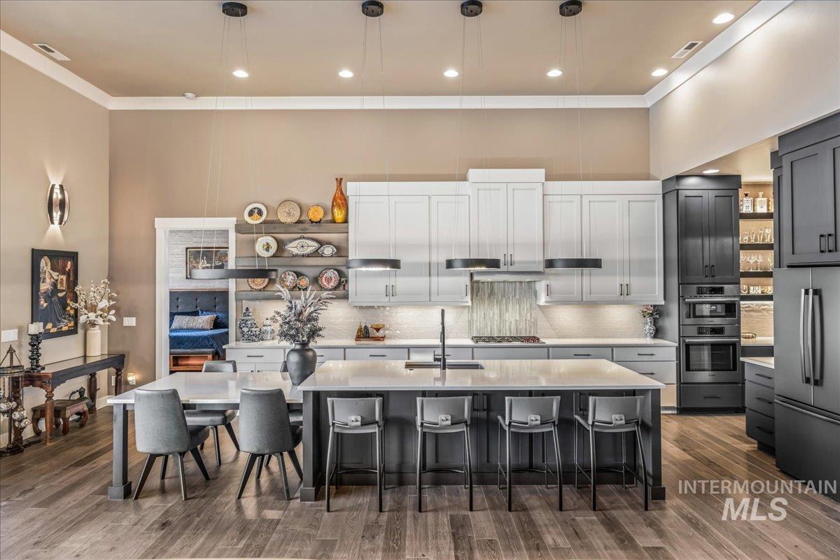 Kitchen with light countertops, appliances with stainless steel finishes, a breakfast bar, dark wood-type flooring, and tasteful backsplash