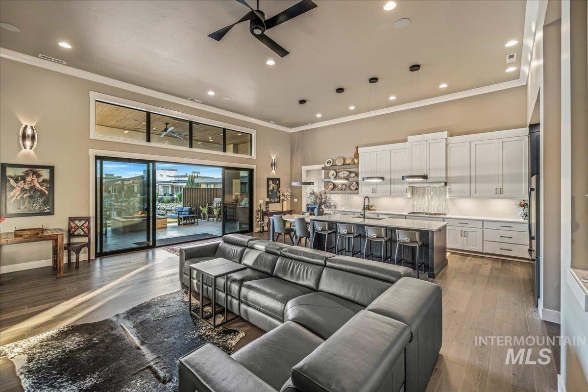 Living room with a ceiling fan, a high ceiling, ornamental molding, dark wood-type flooring, and recessed lighting