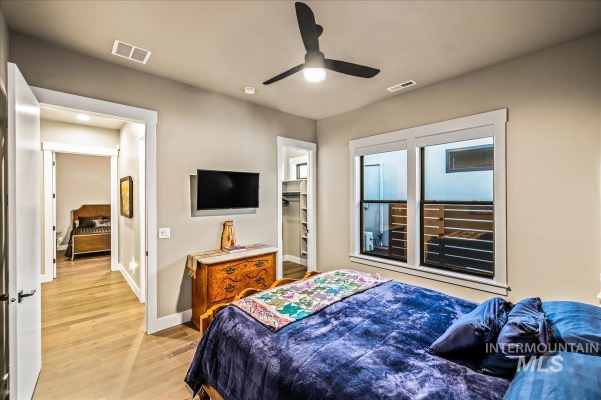 Bedroom with light wood finished floors, a spacious closet, and ceiling fan