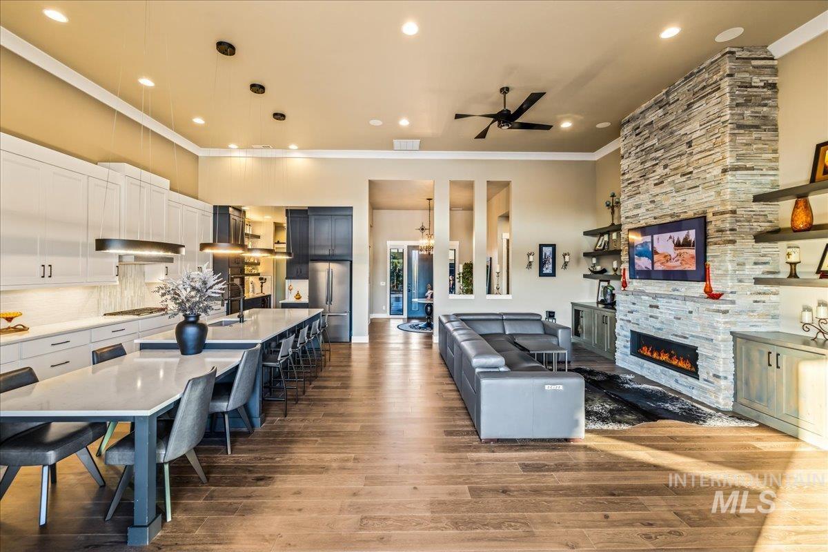Kitchen with crown molding, ceiling fan, a stone fireplace, stainless steel appliances, and wood finished floors