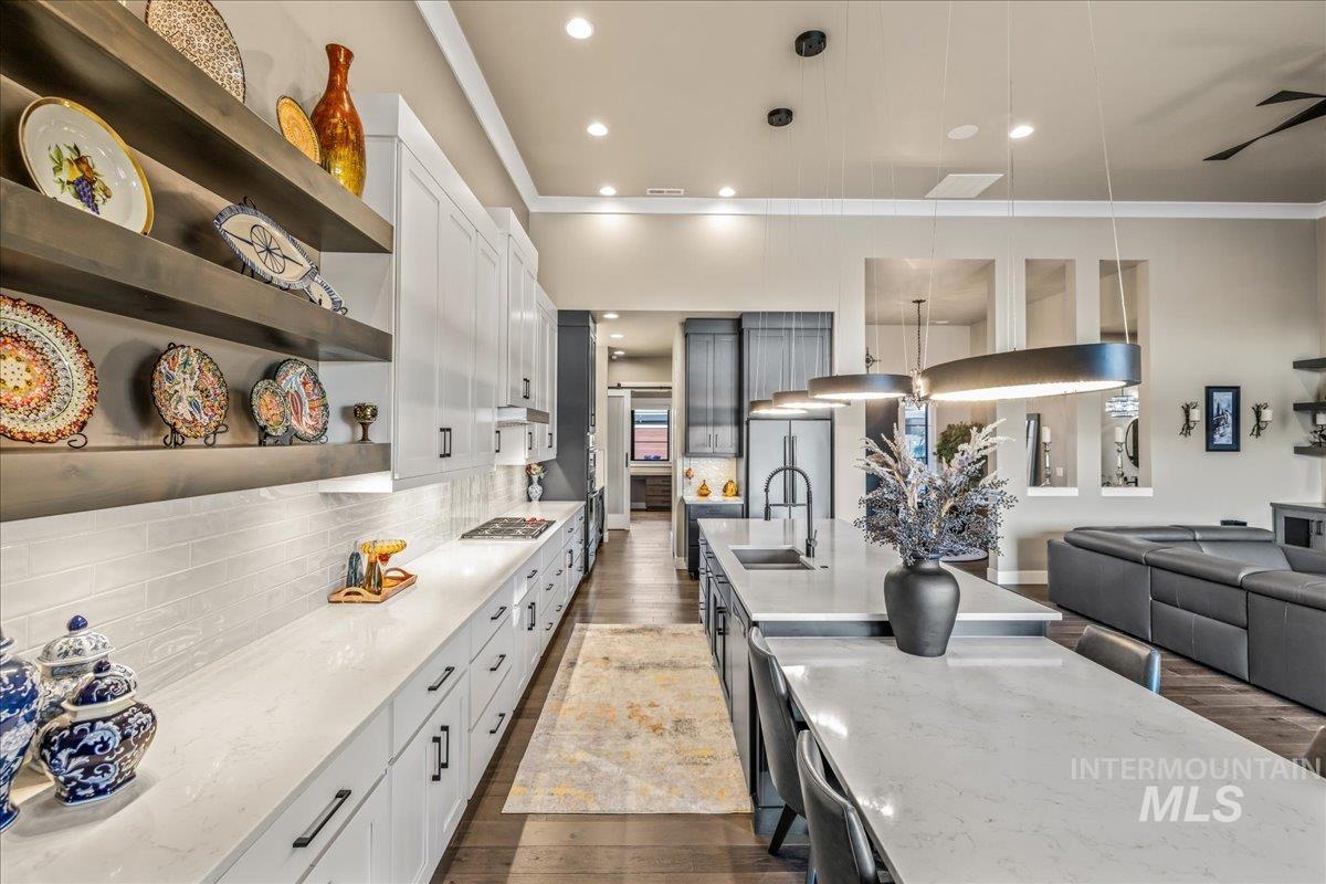 Kitchen featuring open shelves, crown molding, dark wood-style floors, backsplash, and light stone countertops