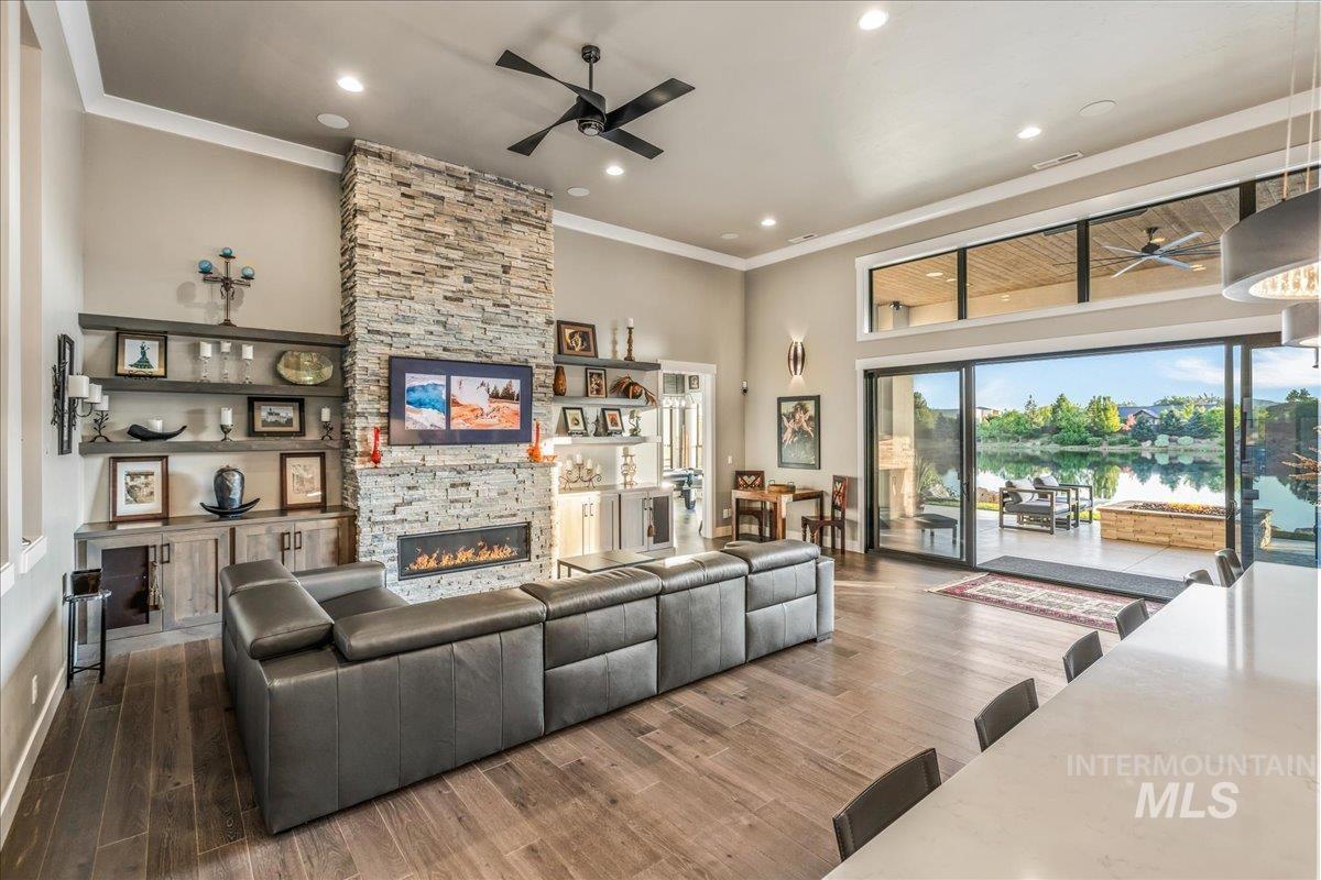 Living area with ceiling fan, ornamental molding, a fireplace, wood finished floors, and a water view