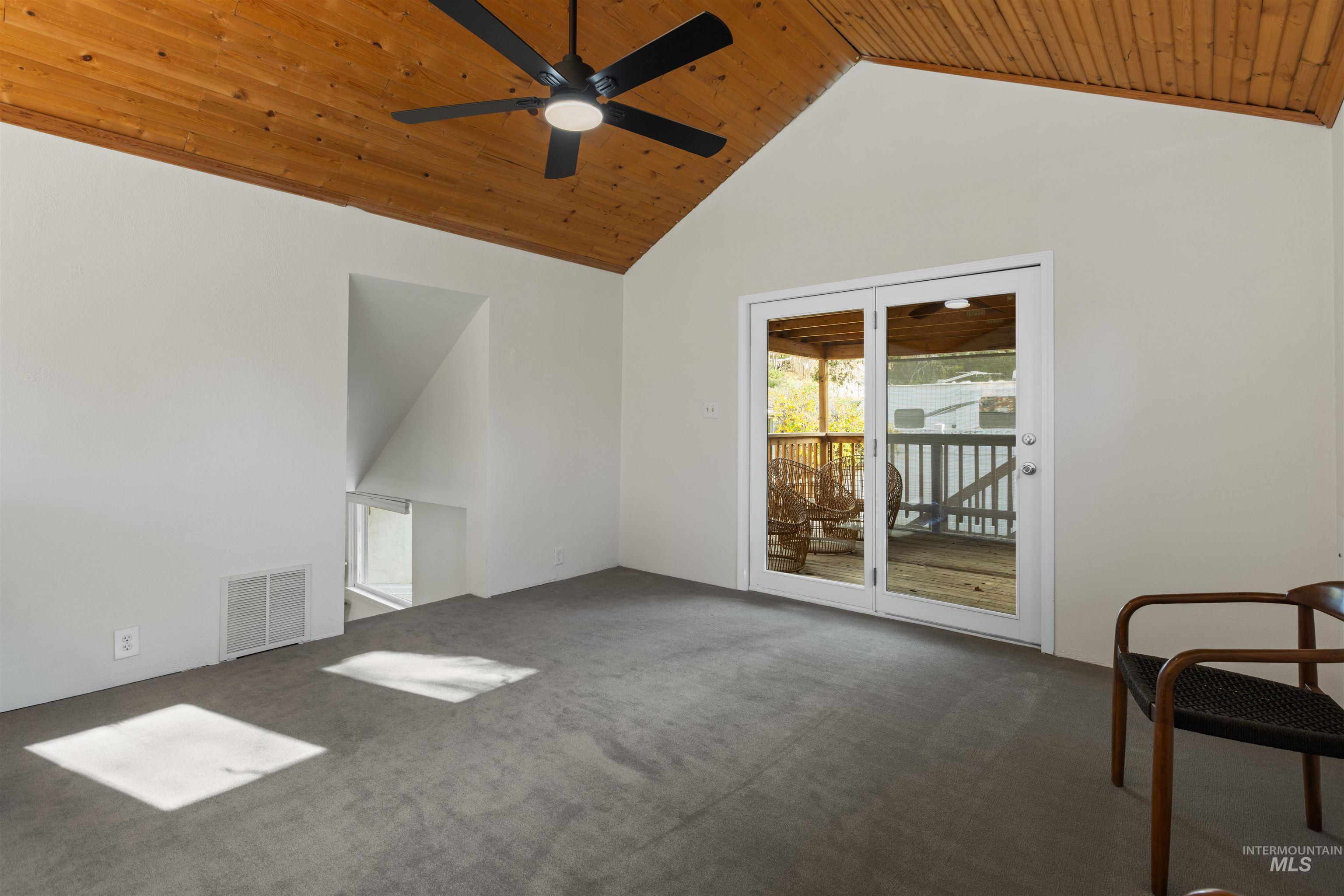 Empty room featuring wood ceiling, dark carpet, high vaulted ceiling, and ceiling fan