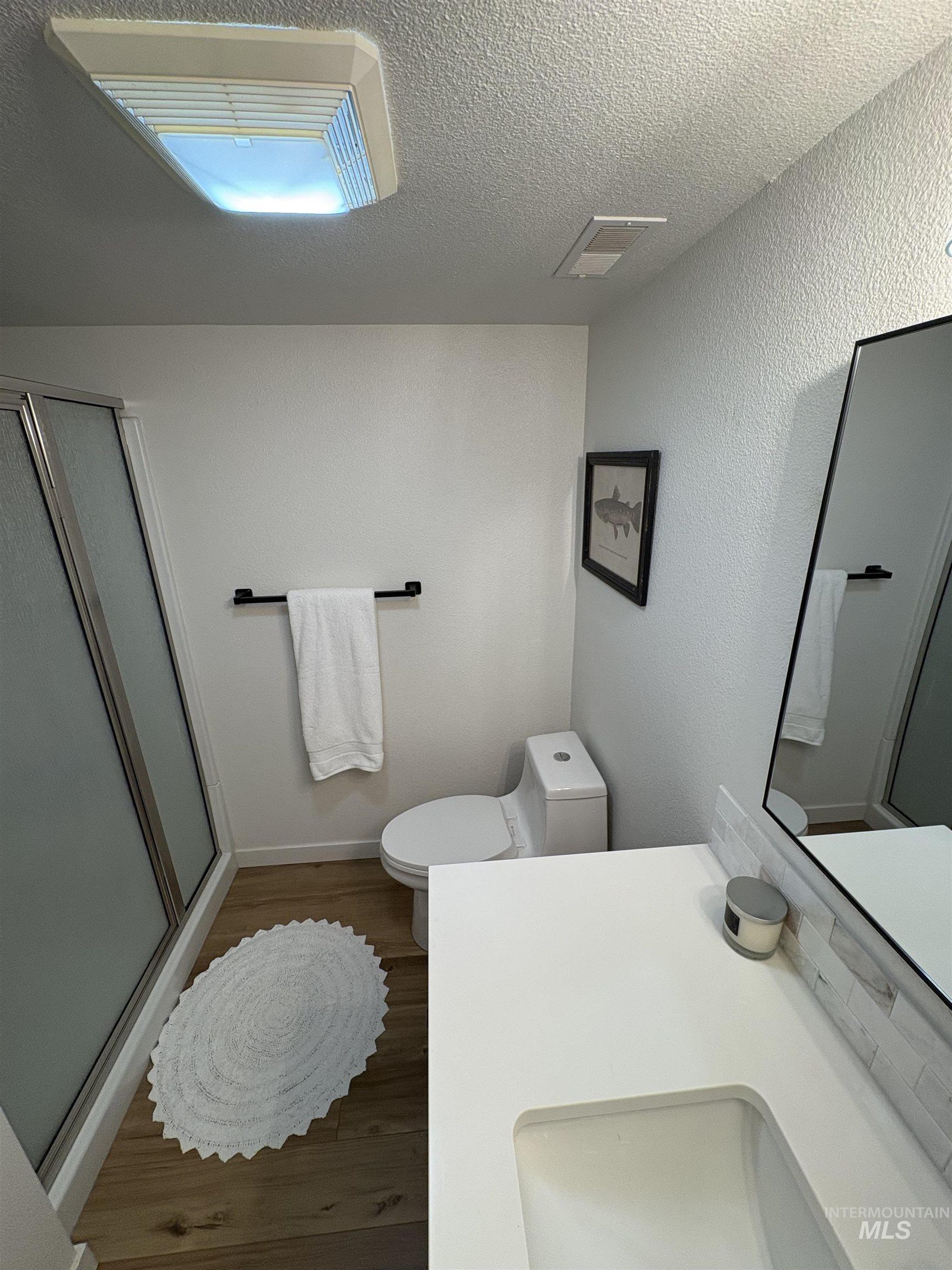 Bathroom with vanity, a shower stall, dark wood-style floors, a textured ceiling, and a textured wall