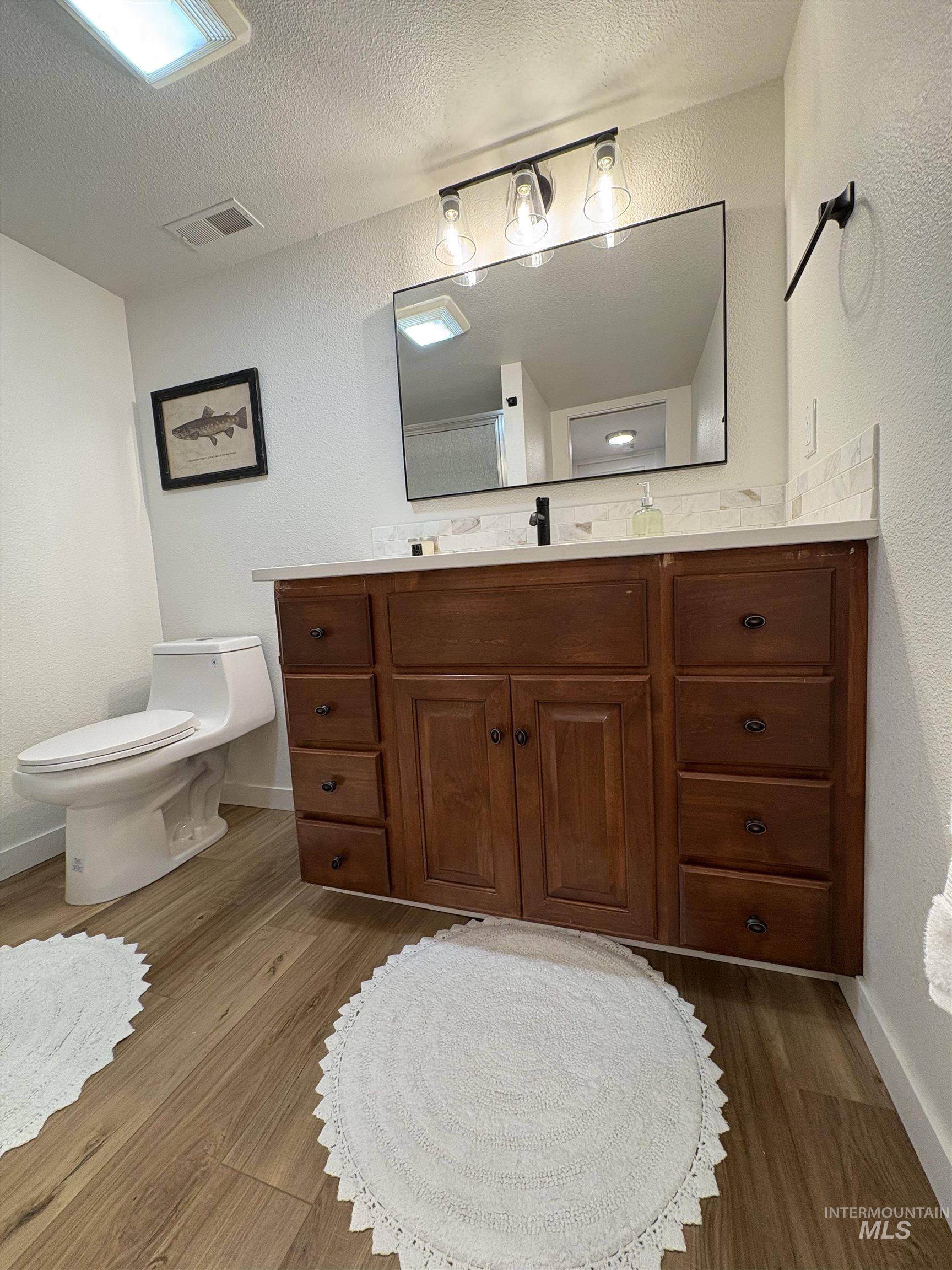 Bathroom with a textured wall, vanity, dark wood finished floors, and a textured ceiling