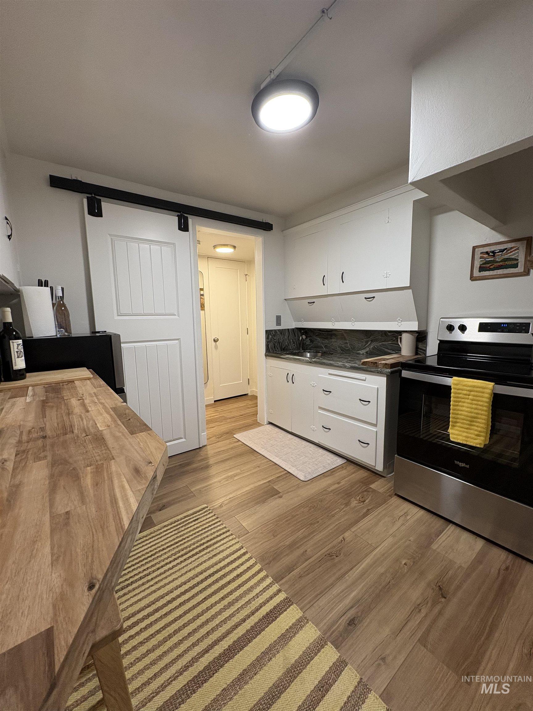 Kitchen featuring a barn door, stainless steel range with electric stovetop, white cabinetry, light wood-style floors, and butcher block counters