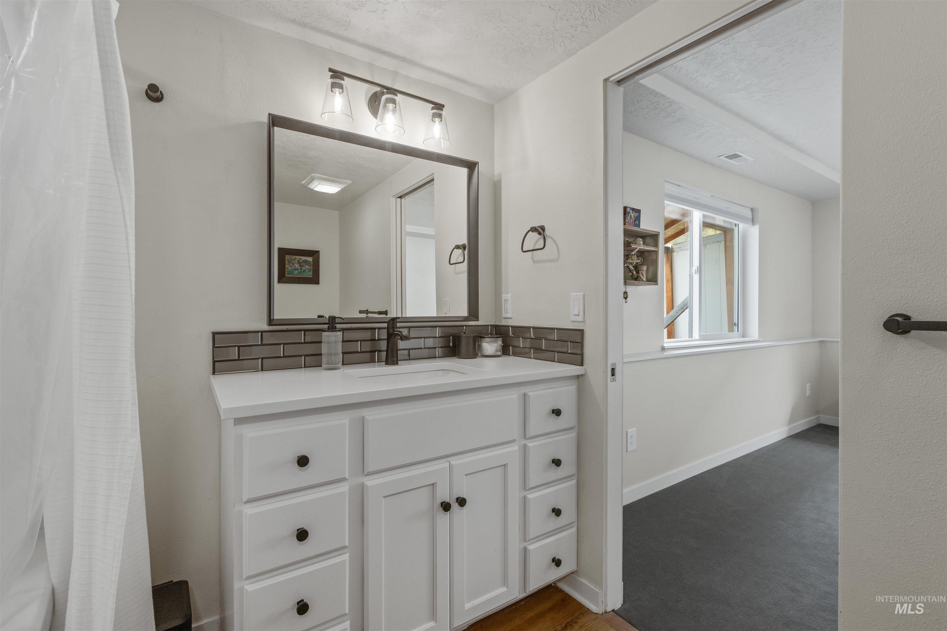 Bathroom featuring curtained shower, vanity, a textured ceiling, tasteful backsplash, and dark wood-style flooring