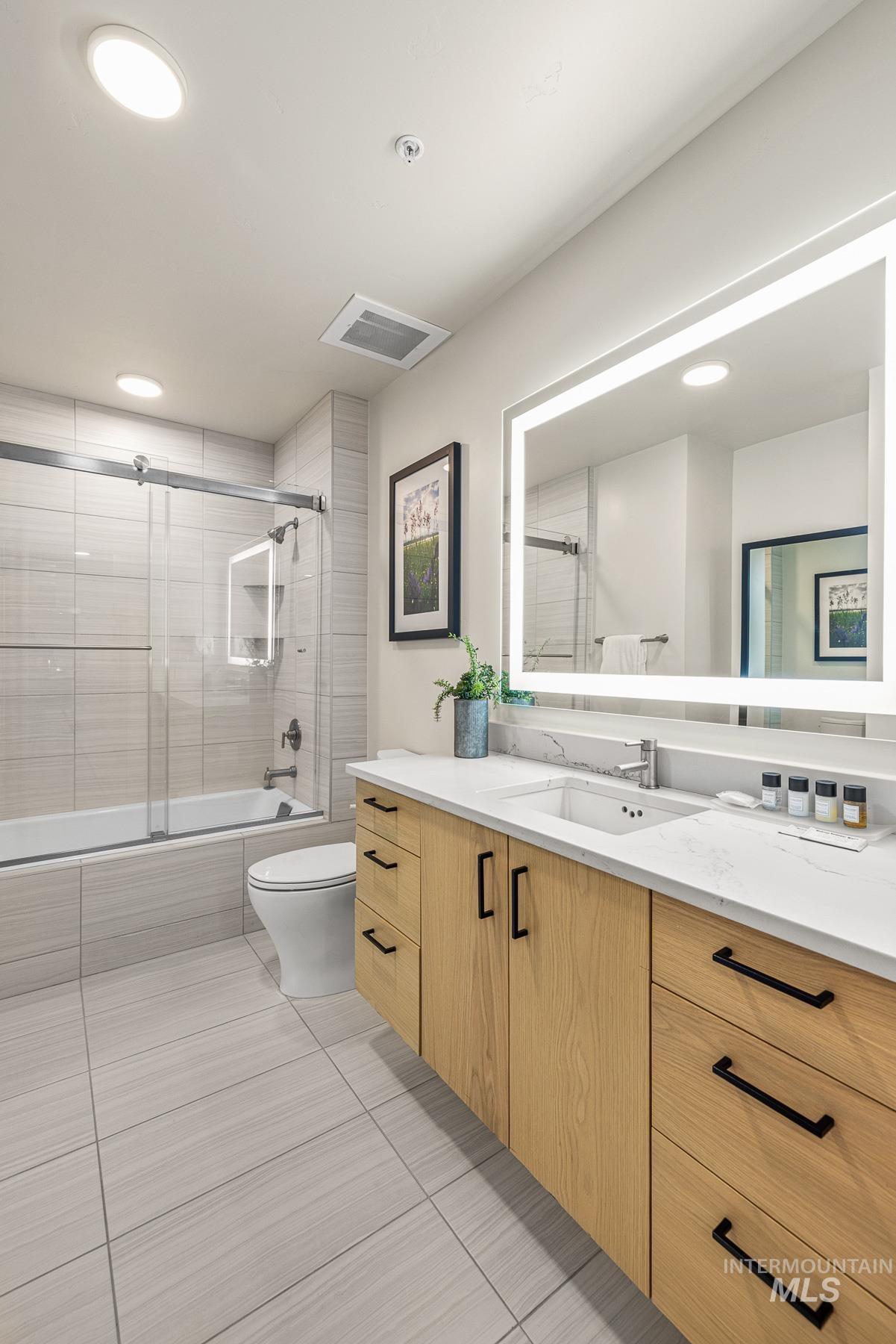 Bathroom with tiled shower, vanity, light tile patterned floors, and recessed lighting
