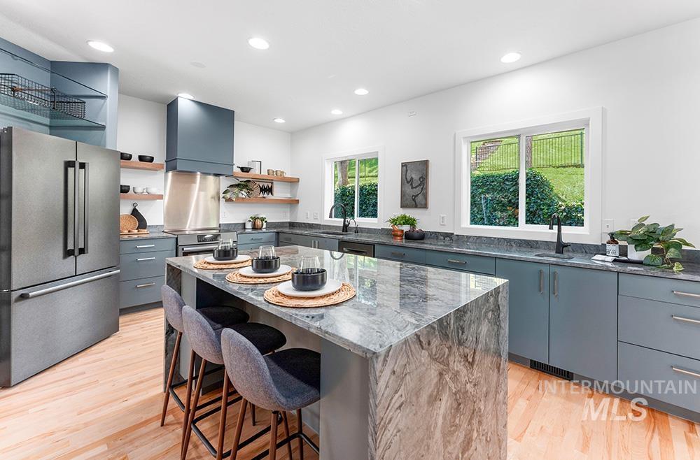Kitchen with appliances with stainless steel finishes, open shelves, wall chimney exhaust hood, a breakfast bar, and light wood finished floors