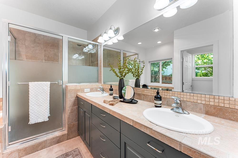 Full bath with double vanity, a stall shower, tasteful backsplash, and tile patterned floors