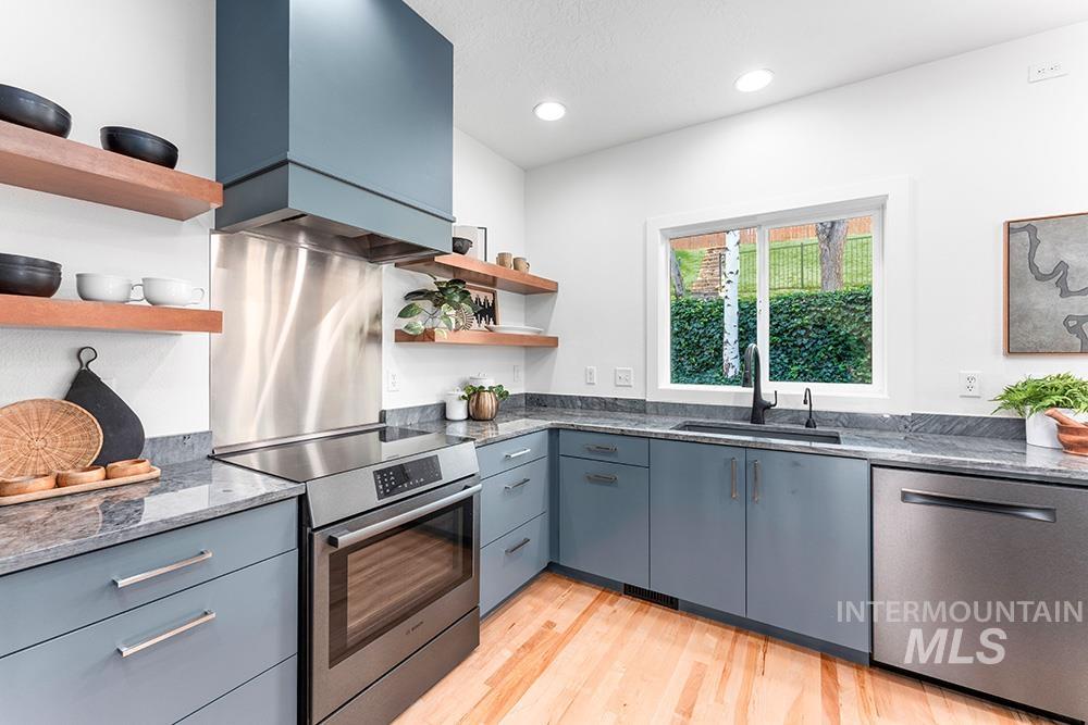 Kitchen featuring open shelves, appliances with stainless steel finishes, light wood finished floors, dark stone counters, and recessed lighting