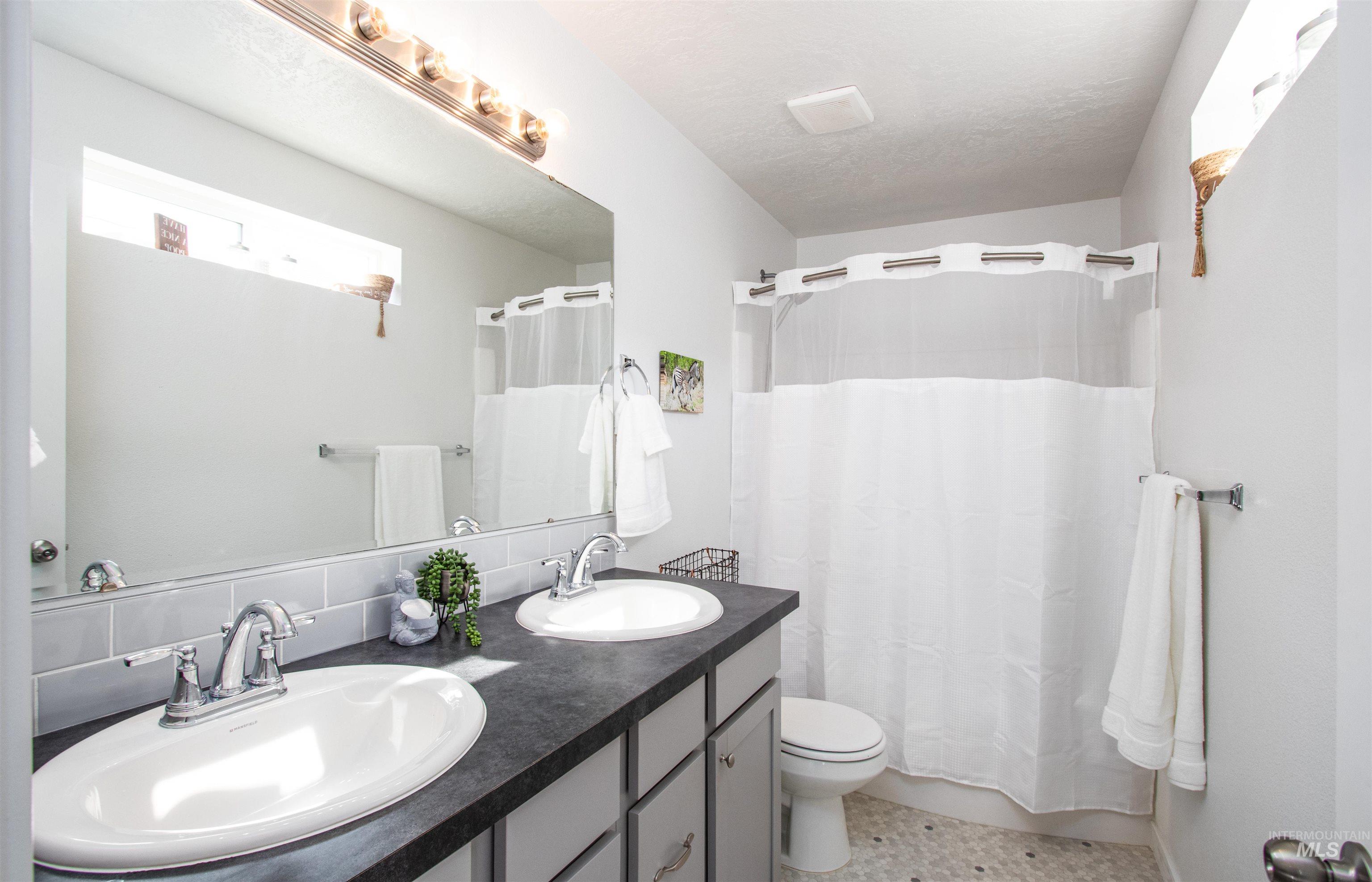 Full bathroom with double vanity, light tile patterned floors, shower / bath combo, and decorative backsplash