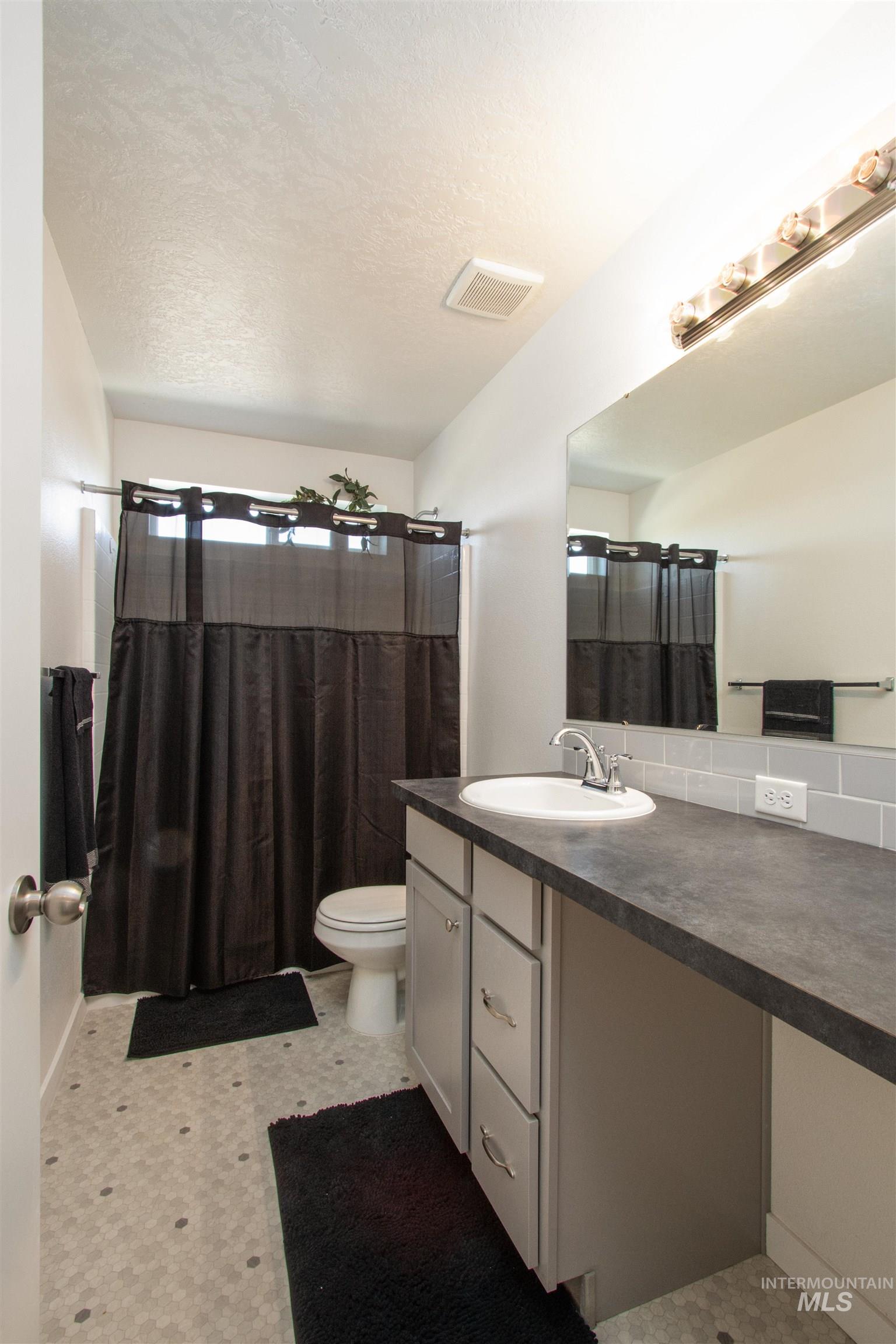 Full bathroom featuring vanity, a textured ceiling, light flooring, and a shower with curtain