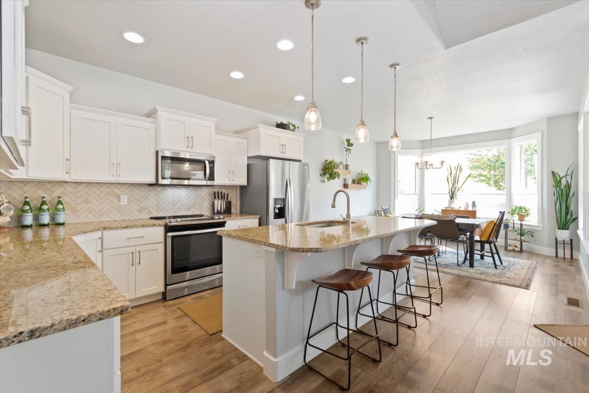 Kitchen featuring appliances with stainless steel finishes, a center island with sink, light stone counters, pendant lighting, and white cabinets