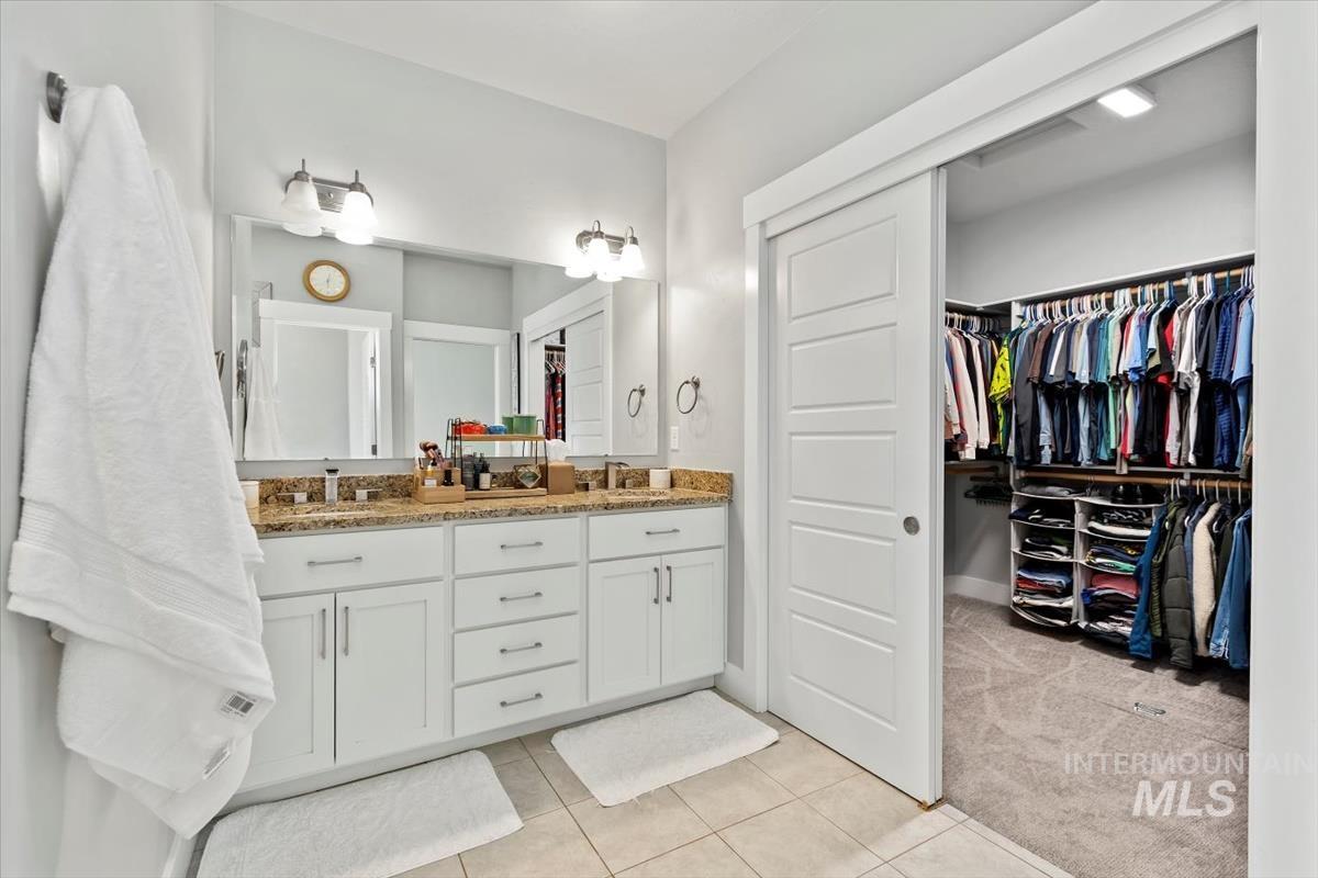 Bathroom with double vanity, light tile patterned floors, and a walk in closet