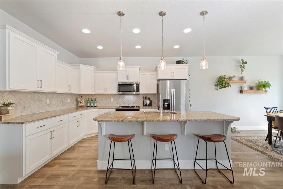 Kitchen featuring stainless steel appliances, tasteful backsplash, white cabinets, hanging light fixtures, and light stone counters