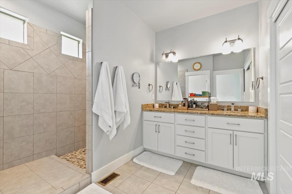 Bathroom featuring double vanity, walk in shower, and light tile patterned floors