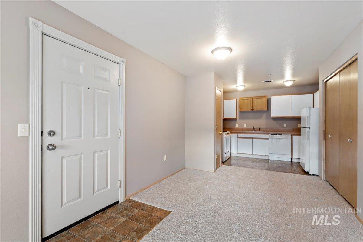 Kitchen featuring white appliances, light carpet, light countertops, light wood finish cabinetry, and white cabinets