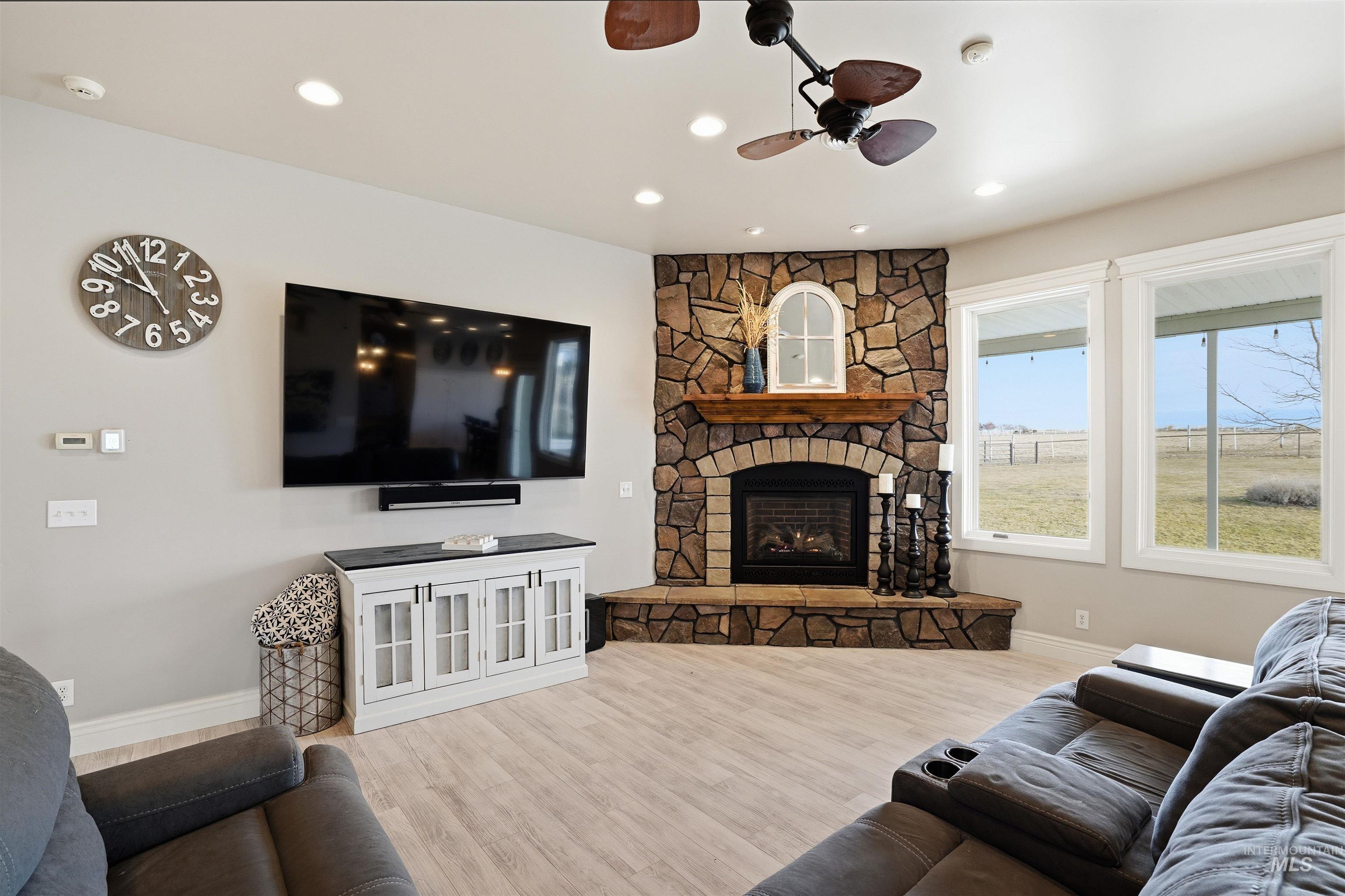 Living room featuring wood finished floors, a stone fireplace, a ceiling fan, and recessed lighting