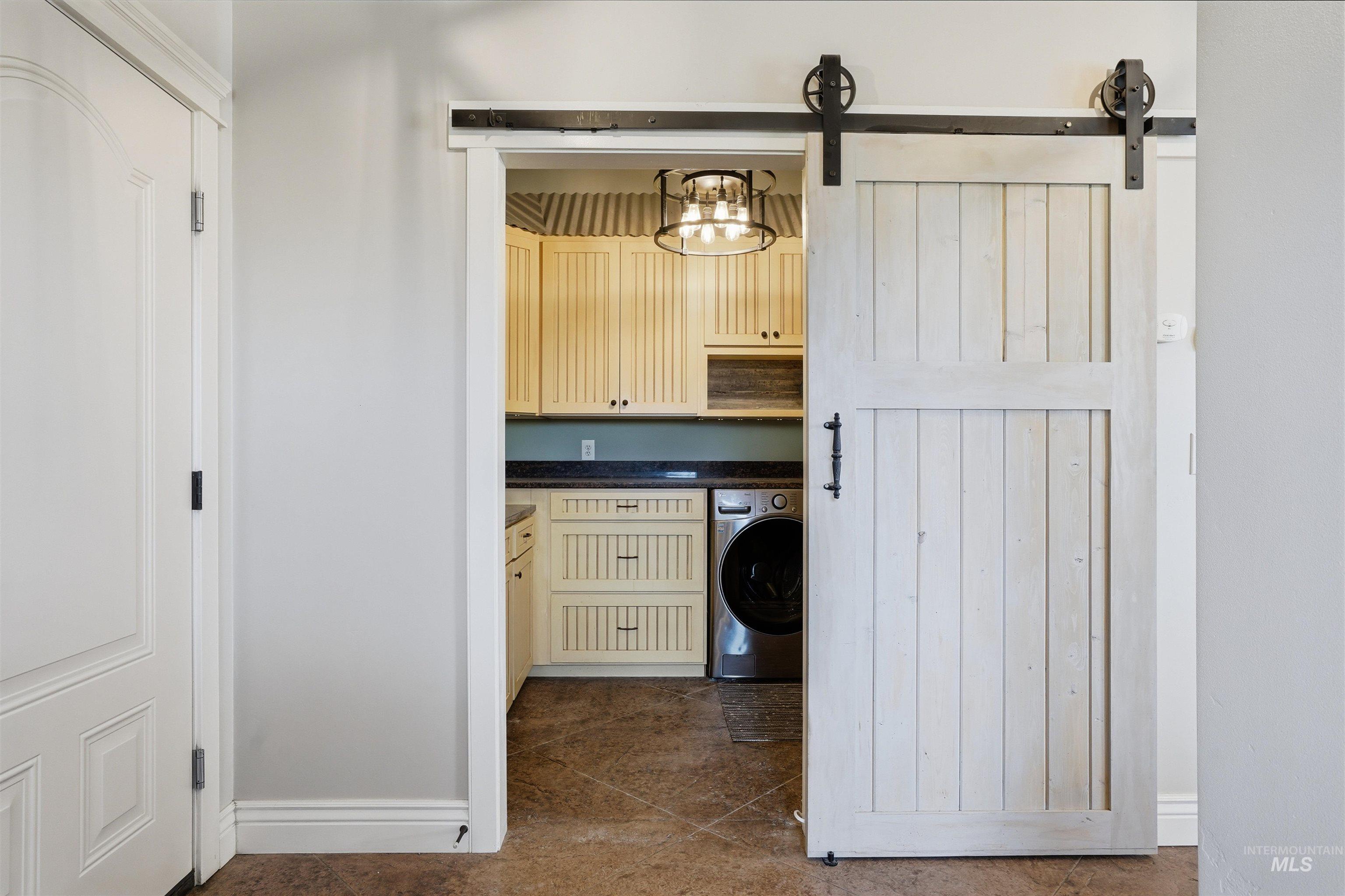 Laundry room featuring washer / clothes dryer, a barn door, cabinet space, suspended lighting, and dark tile patterned floors