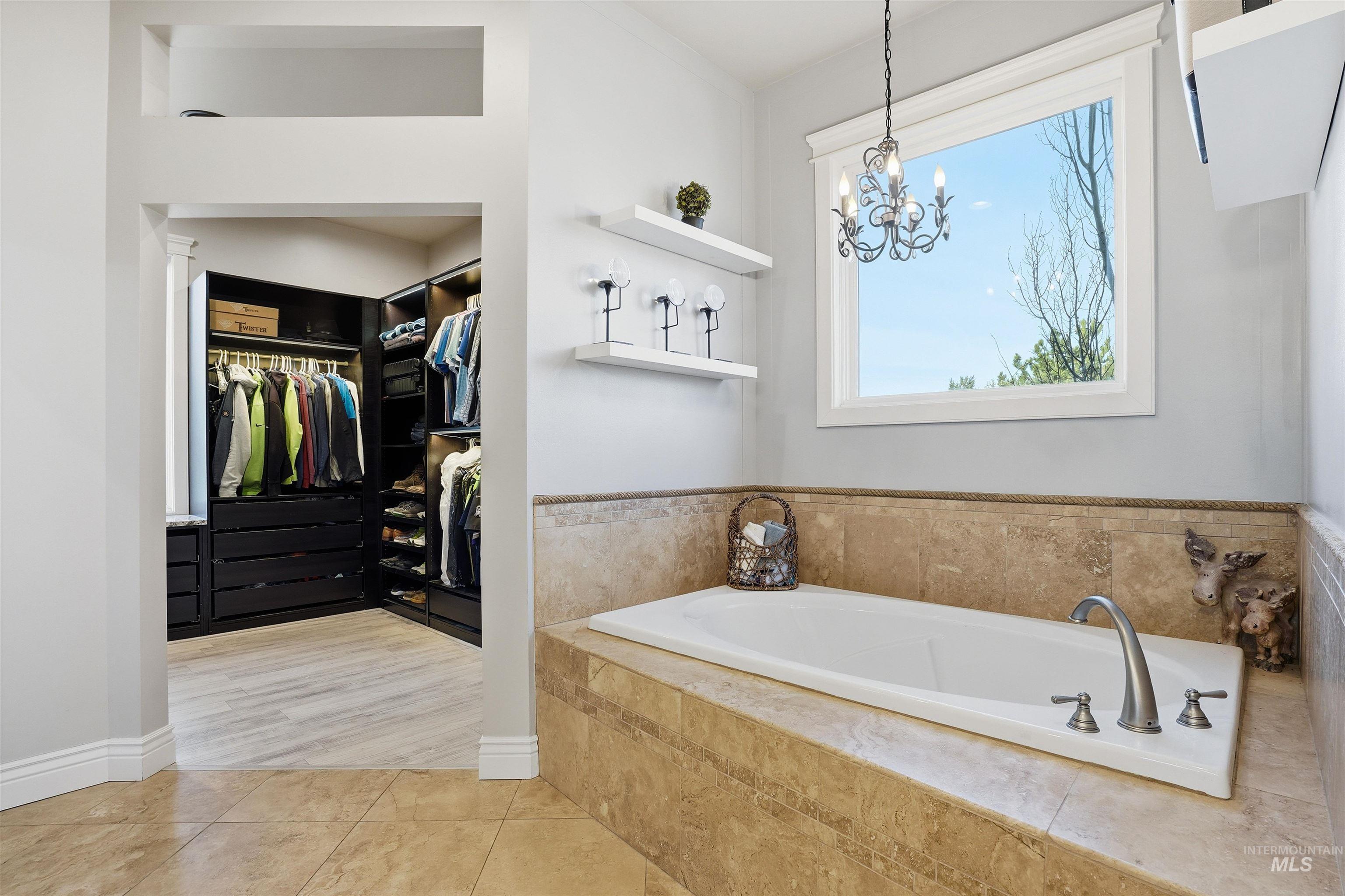 Bathroom featuring a walk in closet, a garden tub, light tile patterned floors, and a chandelier