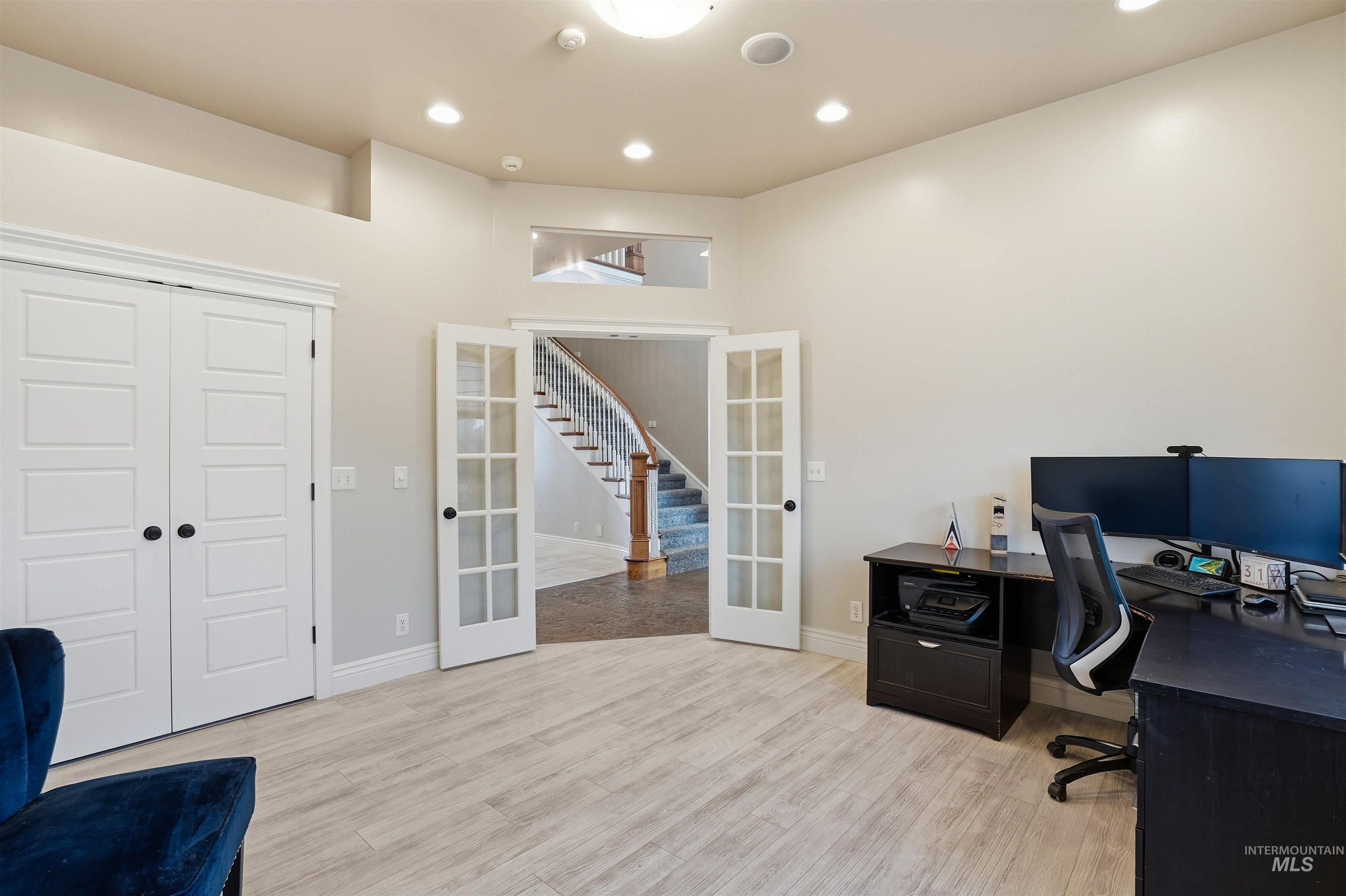 Home office featuring french doors, light wood-style floors, recessed lighting, and a high ceiling