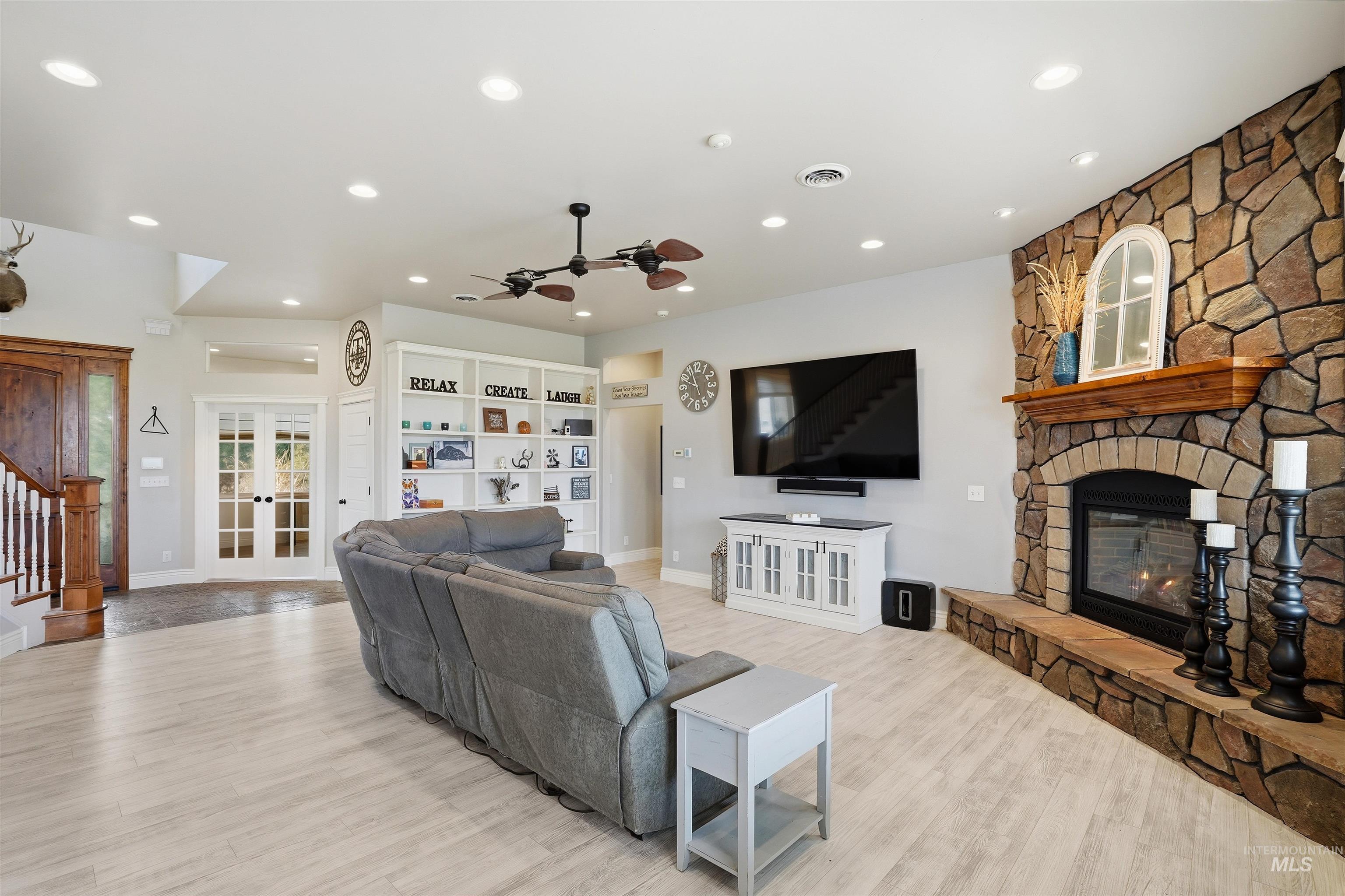 Living room with a ceiling fan, light wood-style floors, recessed lighting, a fireplace, and french doors