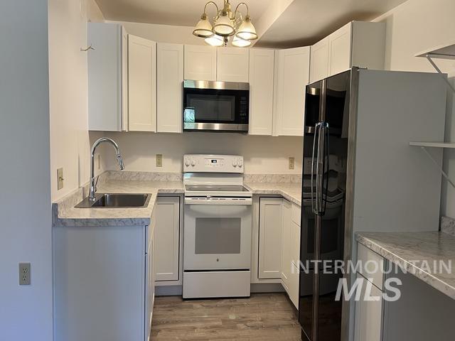 Kitchen with white range with electric cooktop, stainless steel microwave, refrigerator with ice dispenser, a chandelier, and light wood-type flooring