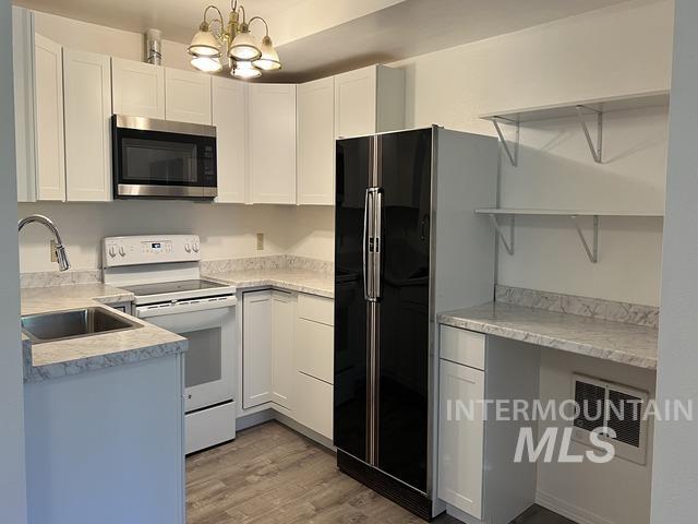 Kitchen featuring stainless steel microwave, electric range, freestanding refrigerator, light wood-style floors, and a chandelier