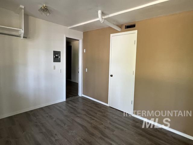 Empty room with dark wood-type flooring and electric panel