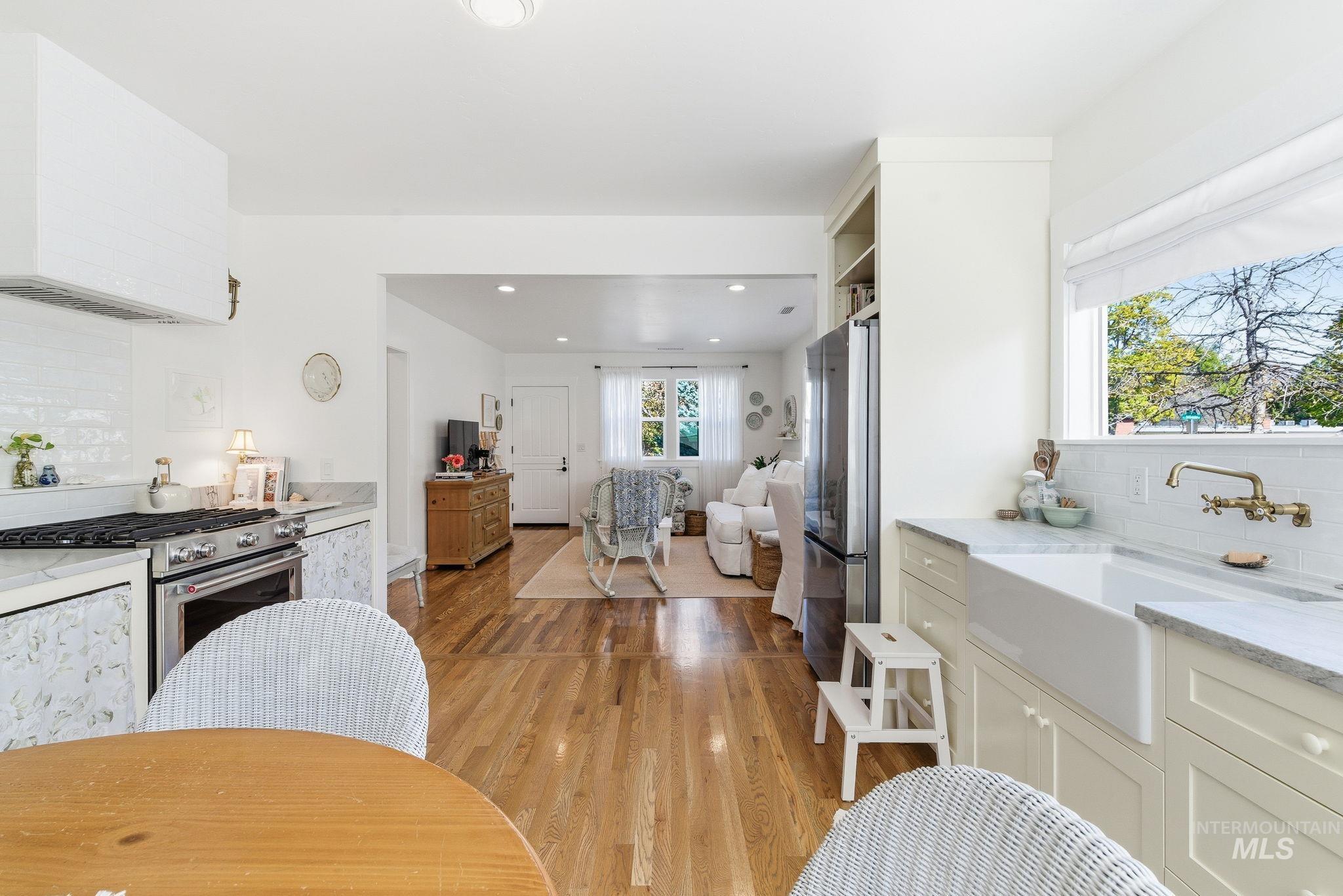 Kitchen featuring backsplash, range hood, light stone counters, stainless steel appliances, and light wood finished floors