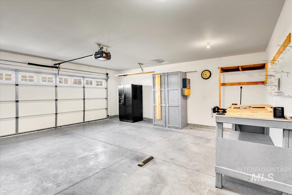Garage with black refrigerator with ice dispenser and a garage door opener