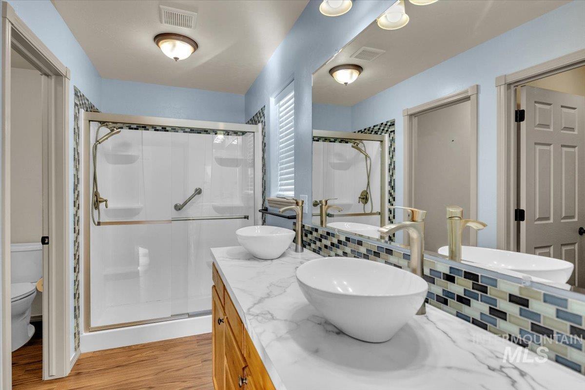 Full bathroom featuring a shower stall, double vanity, and light wood-style floors