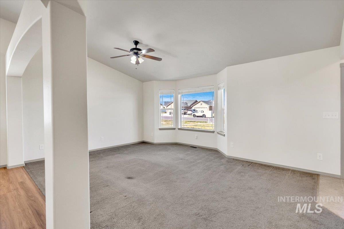 Empty room with light carpet, a ceiling fan, and vaulted ceiling