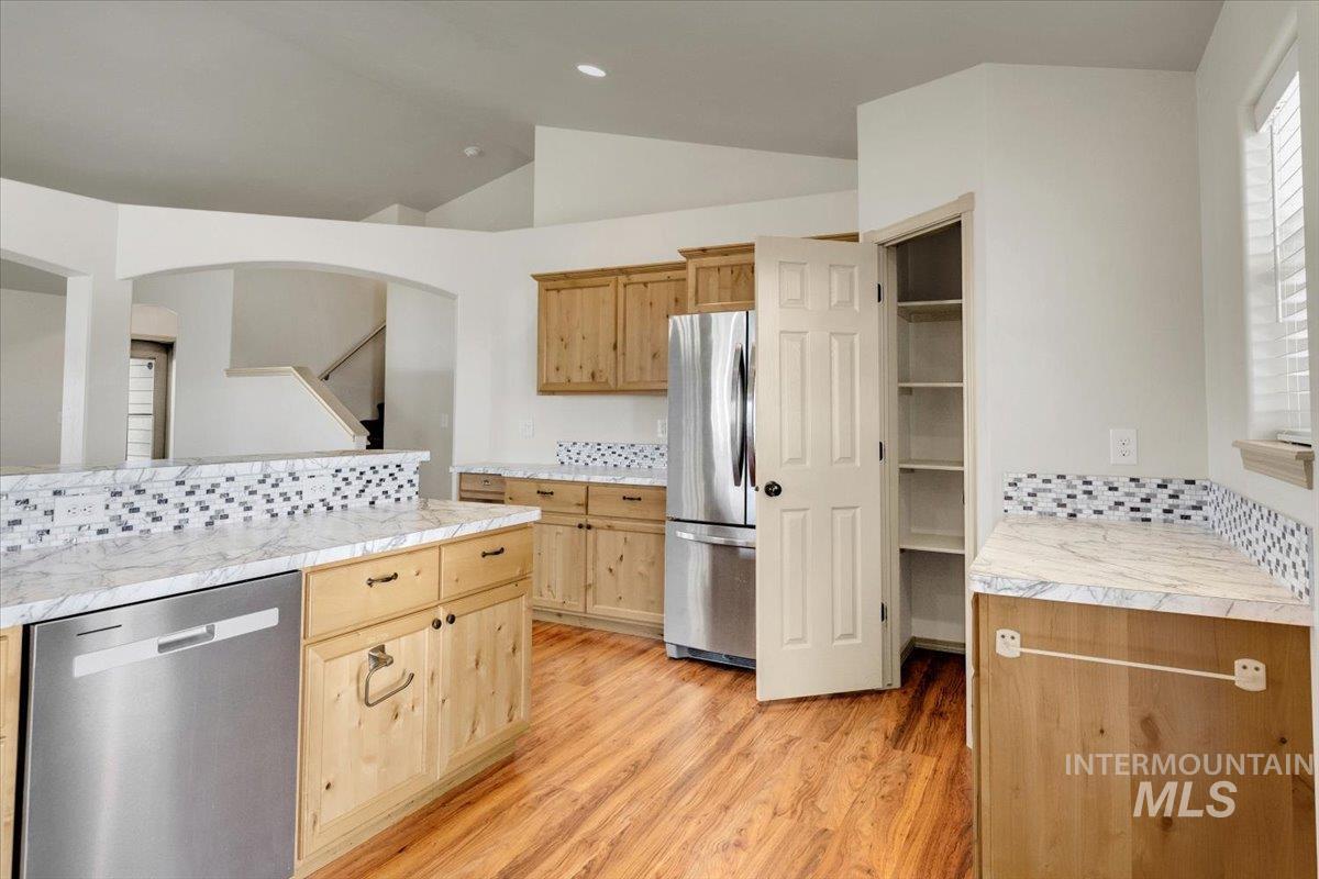 Kitchen with backsplash, light countertops, stainless steel appliances, lofted ceiling, and light wood finished floors
