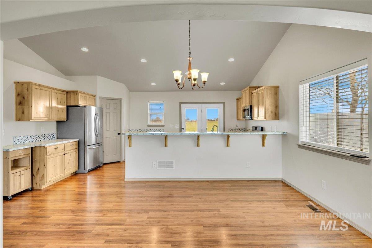 Kitchen with a breakfast bar area, a peninsula, vaulted ceiling, light wood finish cabinets, and suspended lighting