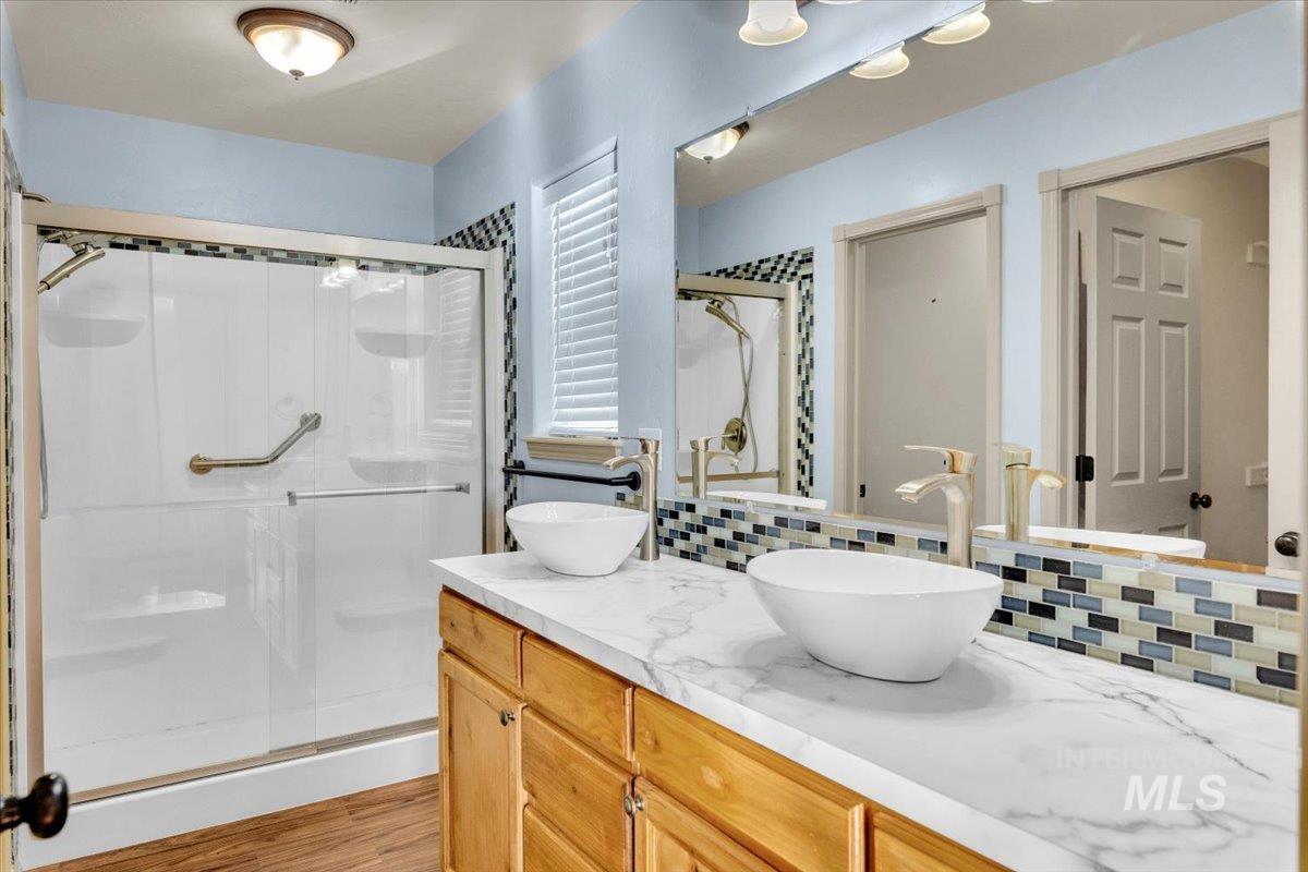 Bathroom with double vanity, a shower stall, tasteful backsplash, and light wood-style floors