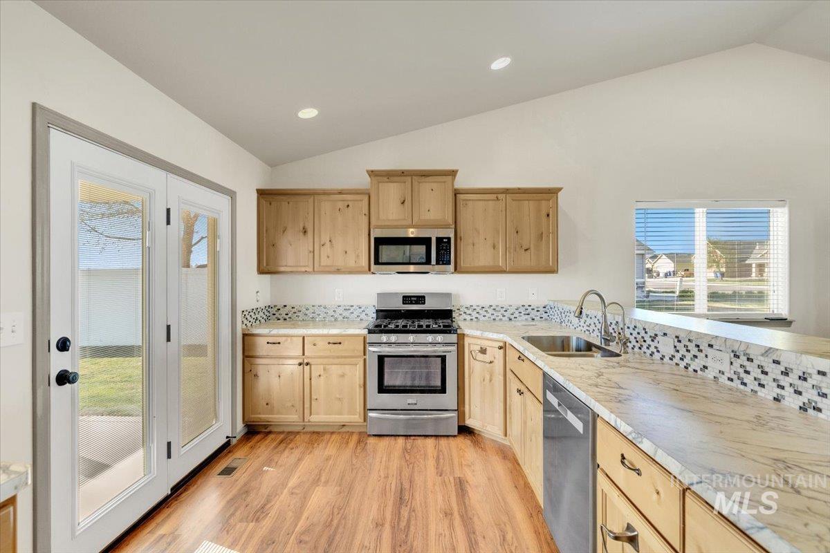 Kitchen with stainless steel appliances, lofted ceiling, light wood finish cabinets, healthy amount of natural light, and recessed lighting