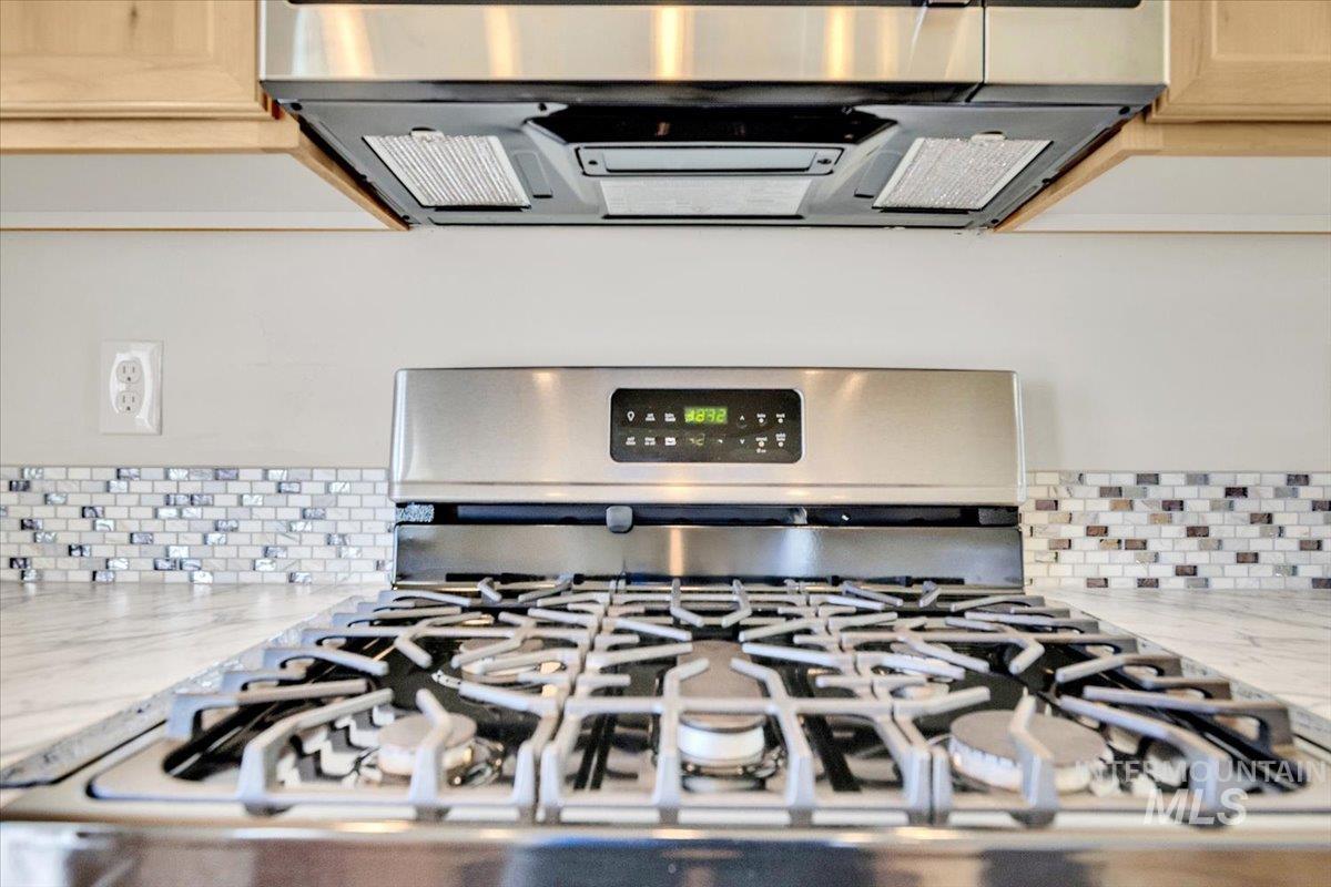Kitchen view of stainless steel appliances, light stone countertops, range hood, and backsplash