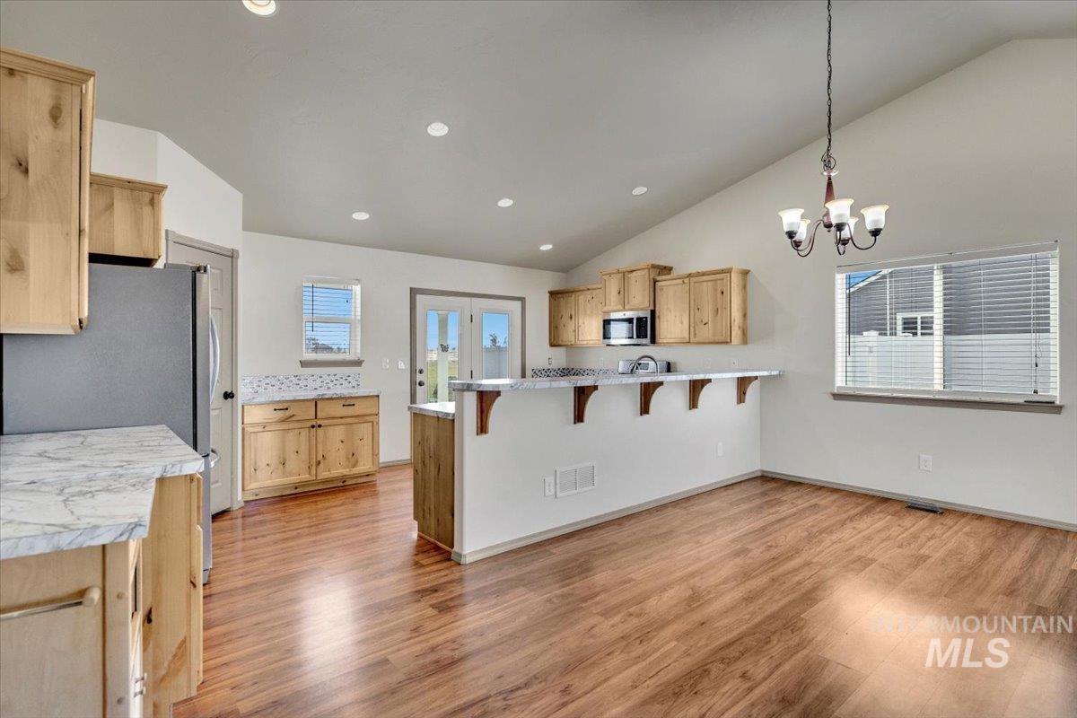 Kitchen with light wood finish cabinetry, a peninsula, a kitchen breakfast bar, light countertops, and stainless steel appliances