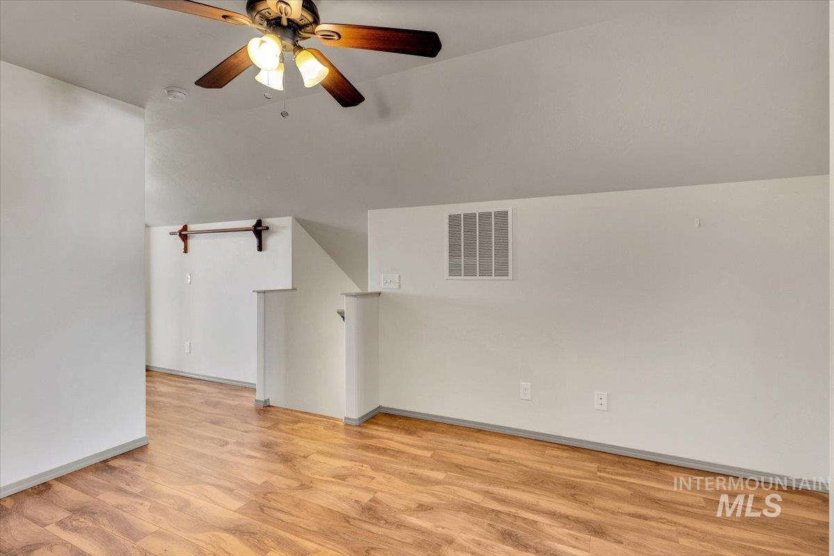 Empty room featuring light wood-type flooring, vaulted ceiling, and ceiling fan