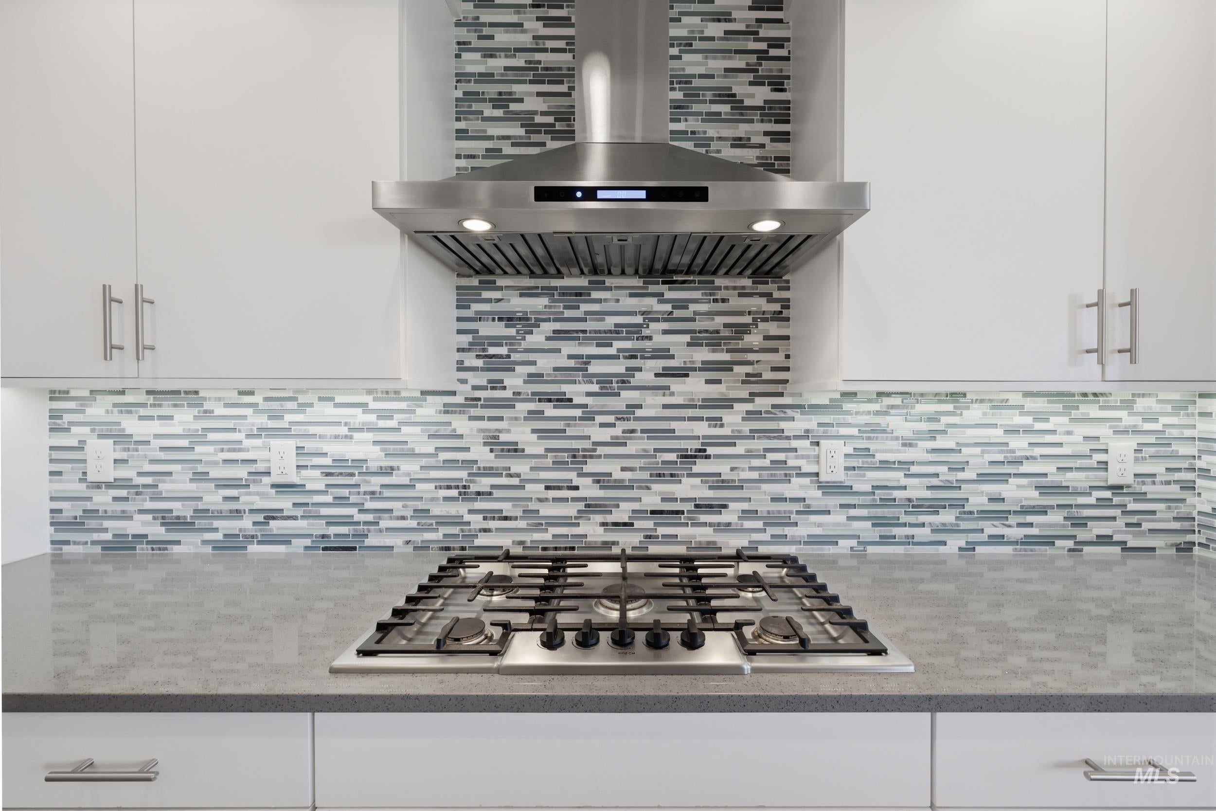 Modern kitchen featuring an integrated gas cooktop with grates, a stainless steel range hood, and white upper and lower cabinetry with brushed nickel hardware