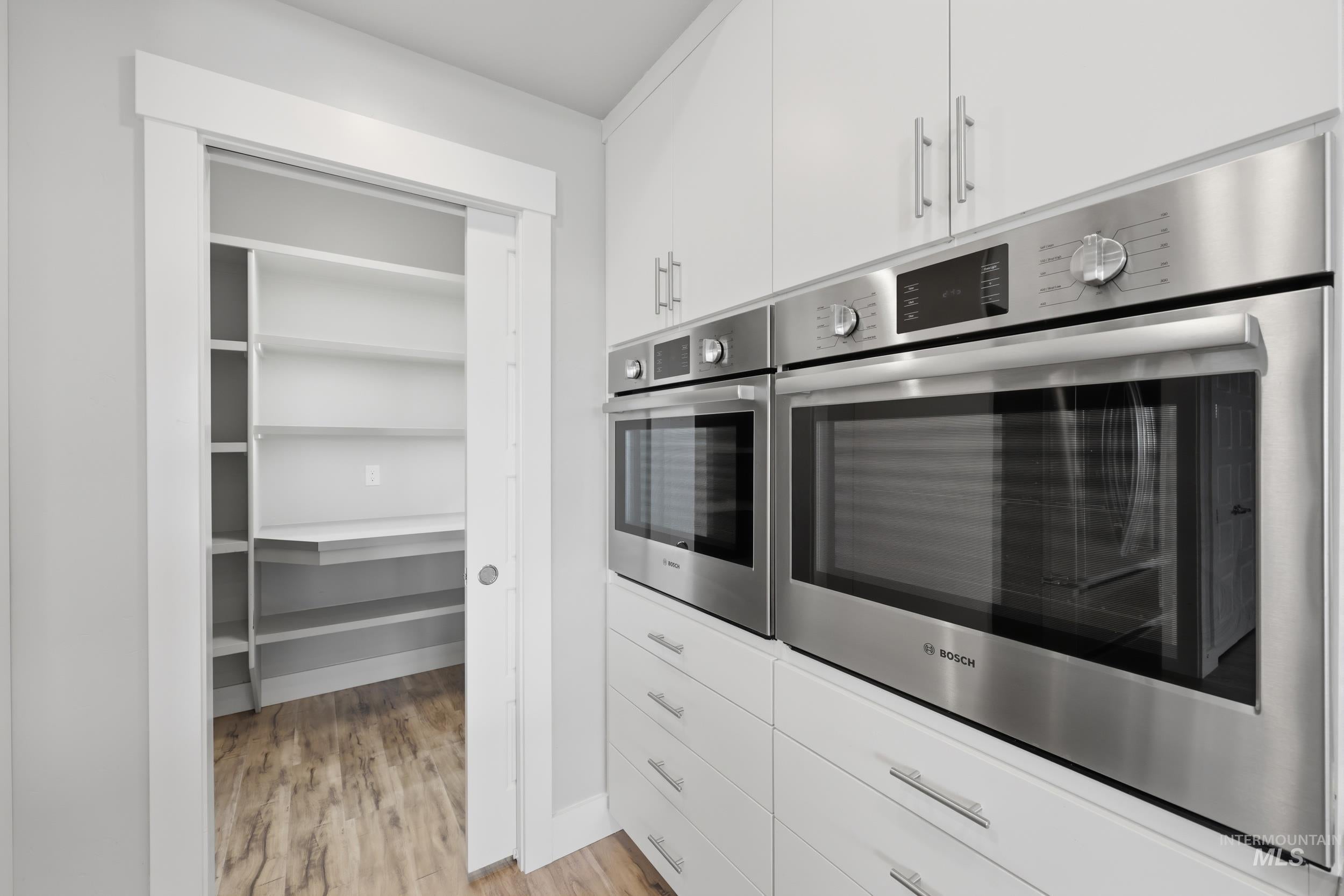 Stainless steel double wall ovens integrated into white cabinetry with brushed nickel hardware