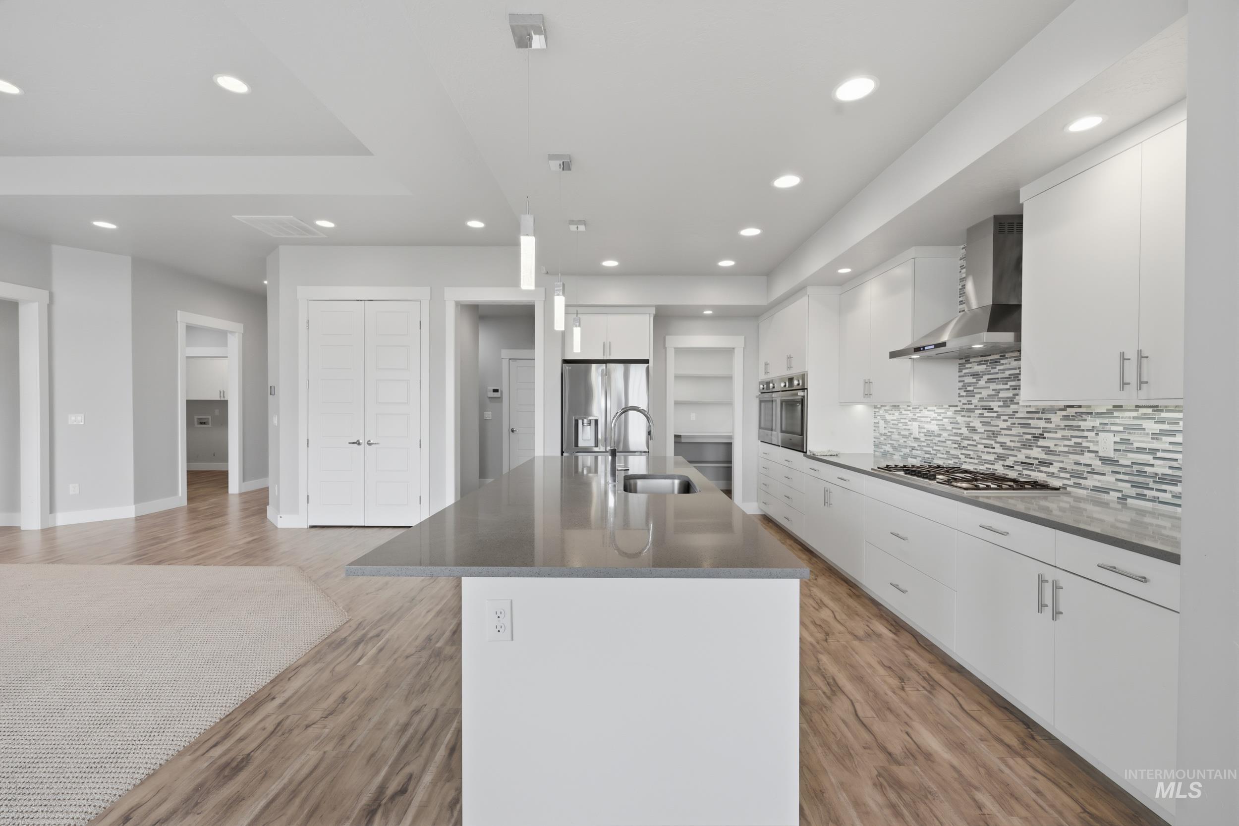 Modern kitchen featuring an expansive center island with an undermount sink, pendant lighting, and stainless steel appliances including a refrigerator, double ovens, and a gas range