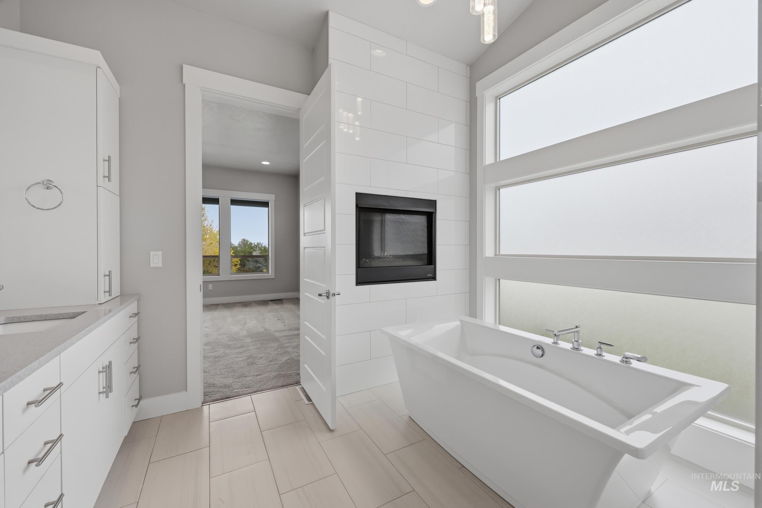 Bathroom featuring a freestanding soaking tub, wall-mounted fireplace, and large privacy windows